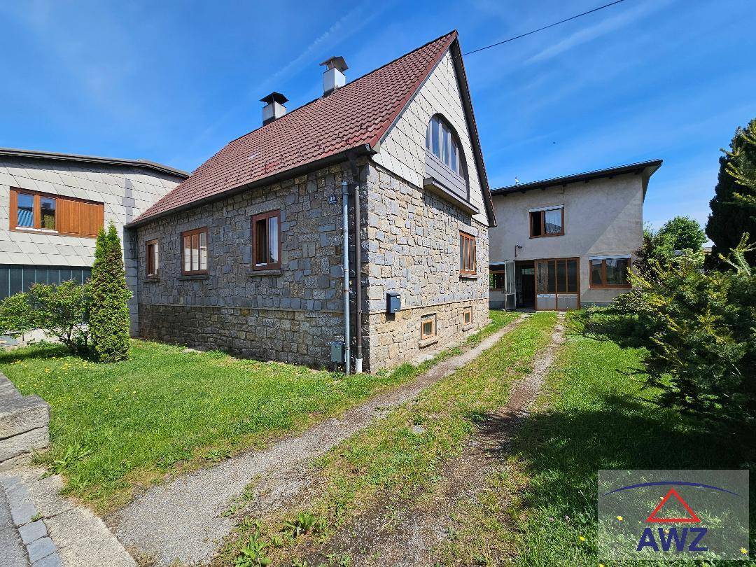 Charmantes Steinhaus mit rotem Ziegeldach, umgeben von einem grünen Rasen und einer Kiesauffahrt.