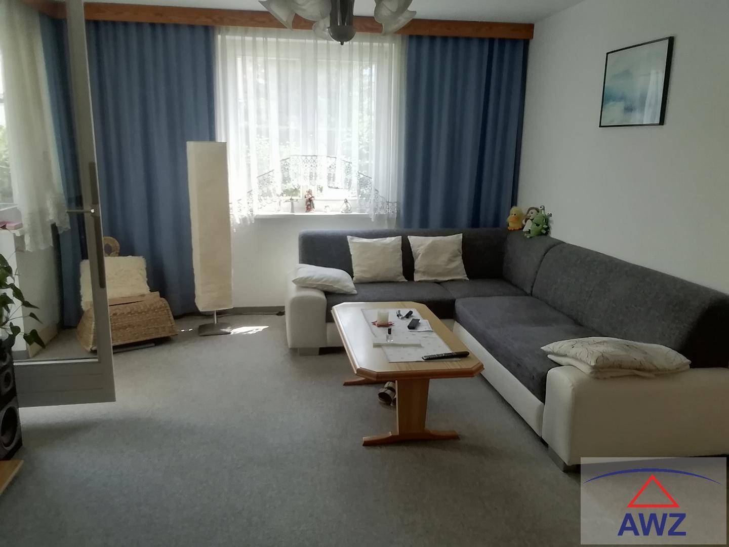 Helles Wohnzimmer mit großem Ecksofa, Couchtisch und blauen Vorhängen, bietet viel Tageslicht.