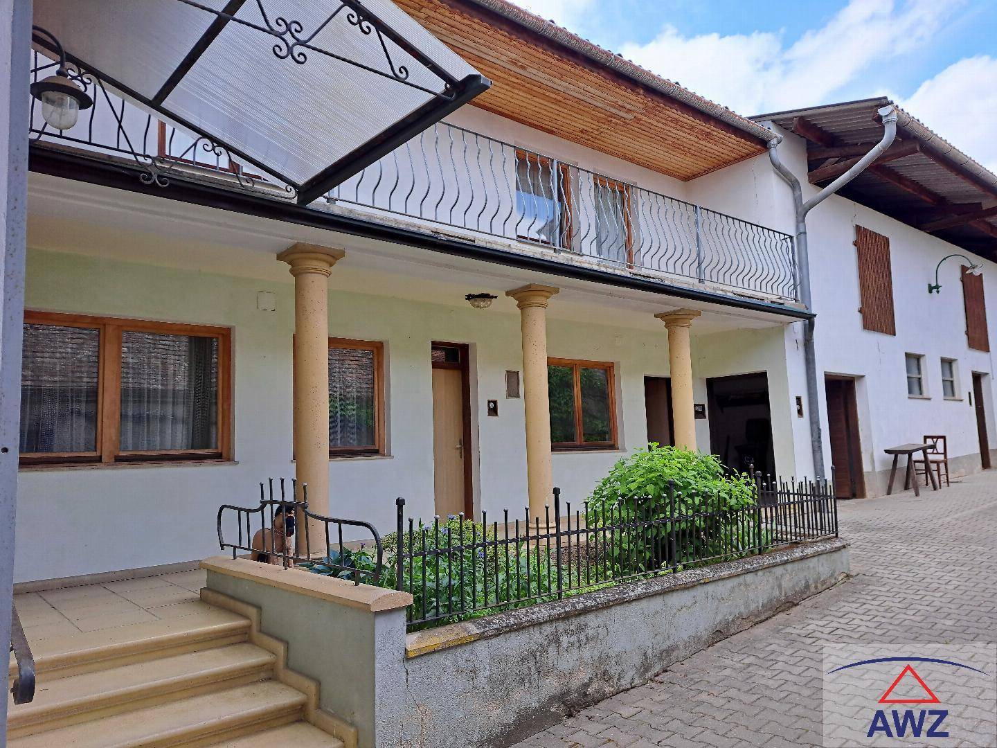 Gebäudefassade mit überdachtem Eingangsbereich, Säulen und einem Balkon im Obergeschoss.