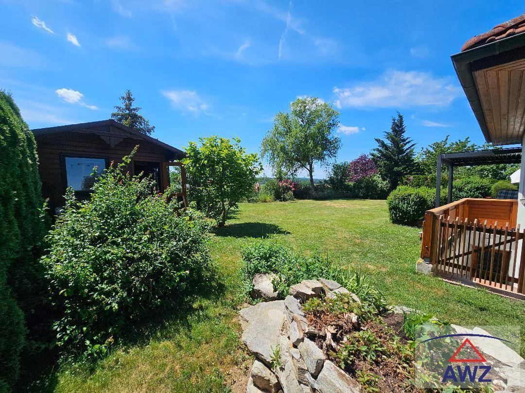 Gepflegter Garten mit einem kleinen Gartenhaus, Sträuchern und weitem Blick in die Landschaft.