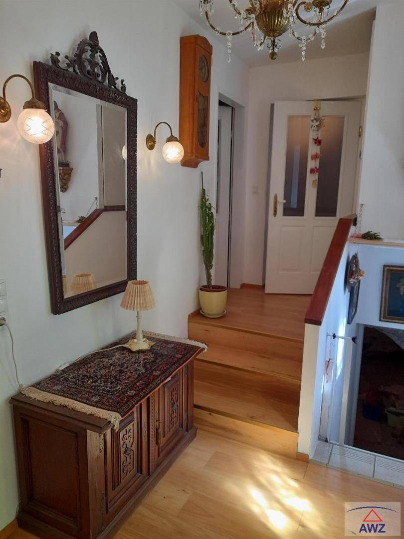 Heller Eingangsbereich mit Holztreppe, einem großen Spiegel und traditionellen Möbeln.