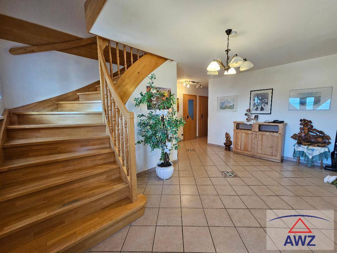 Heller Eingangsbereich mit einer eleganten Holztreppe, Fliesenboden und traditioneller Einrichtung.