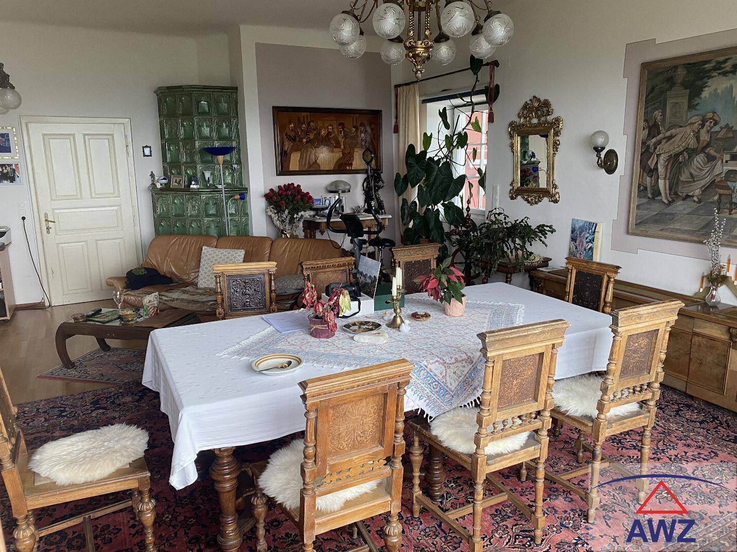 Traditioneller Essbereich mit großem Holztisch, verzierten Stühlen und einem grünen Kachelofen.