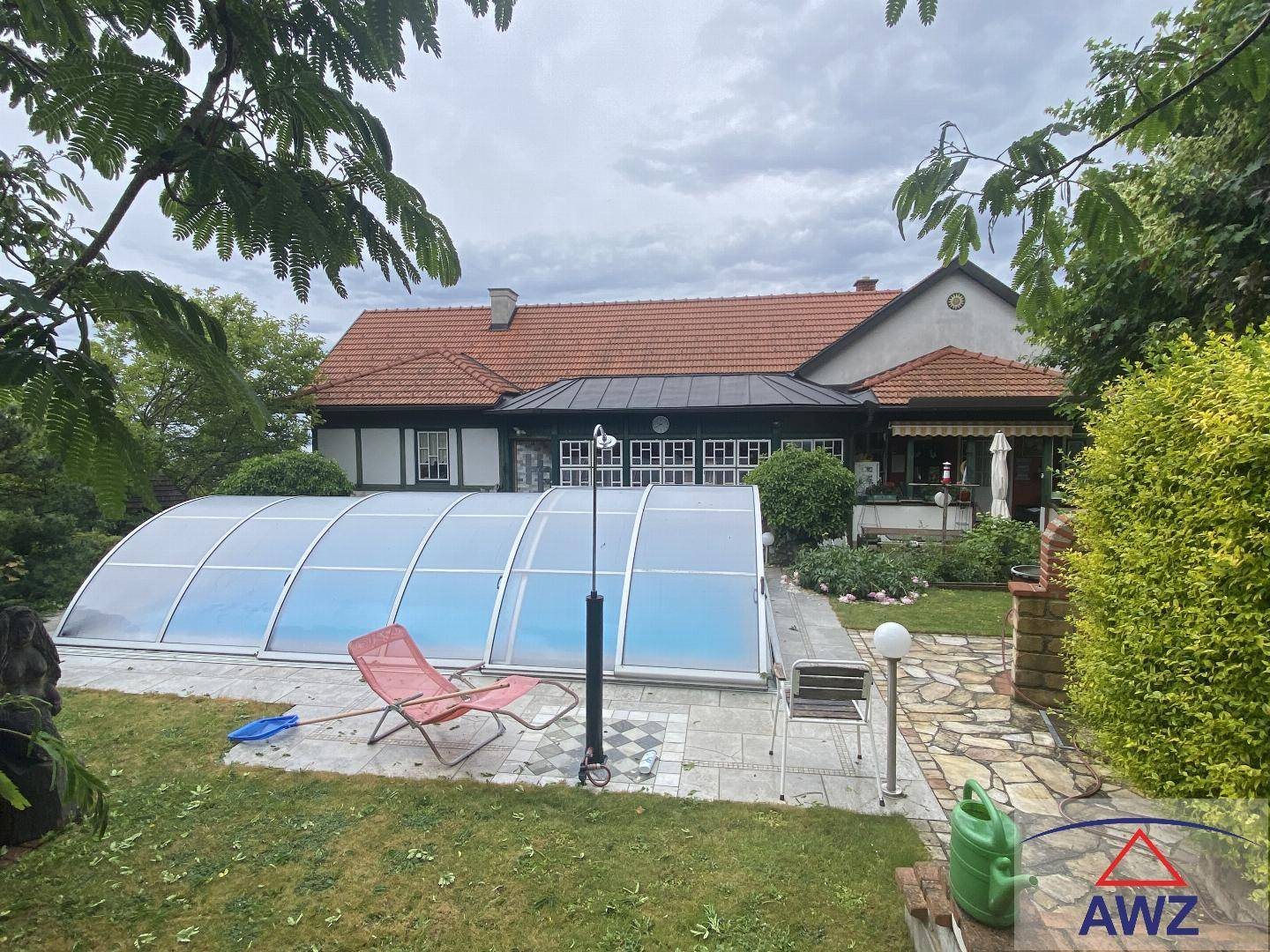 Außenansicht des Hauses mit überdachtem Pool und Gartenbereich unter bewölktem Himmel.