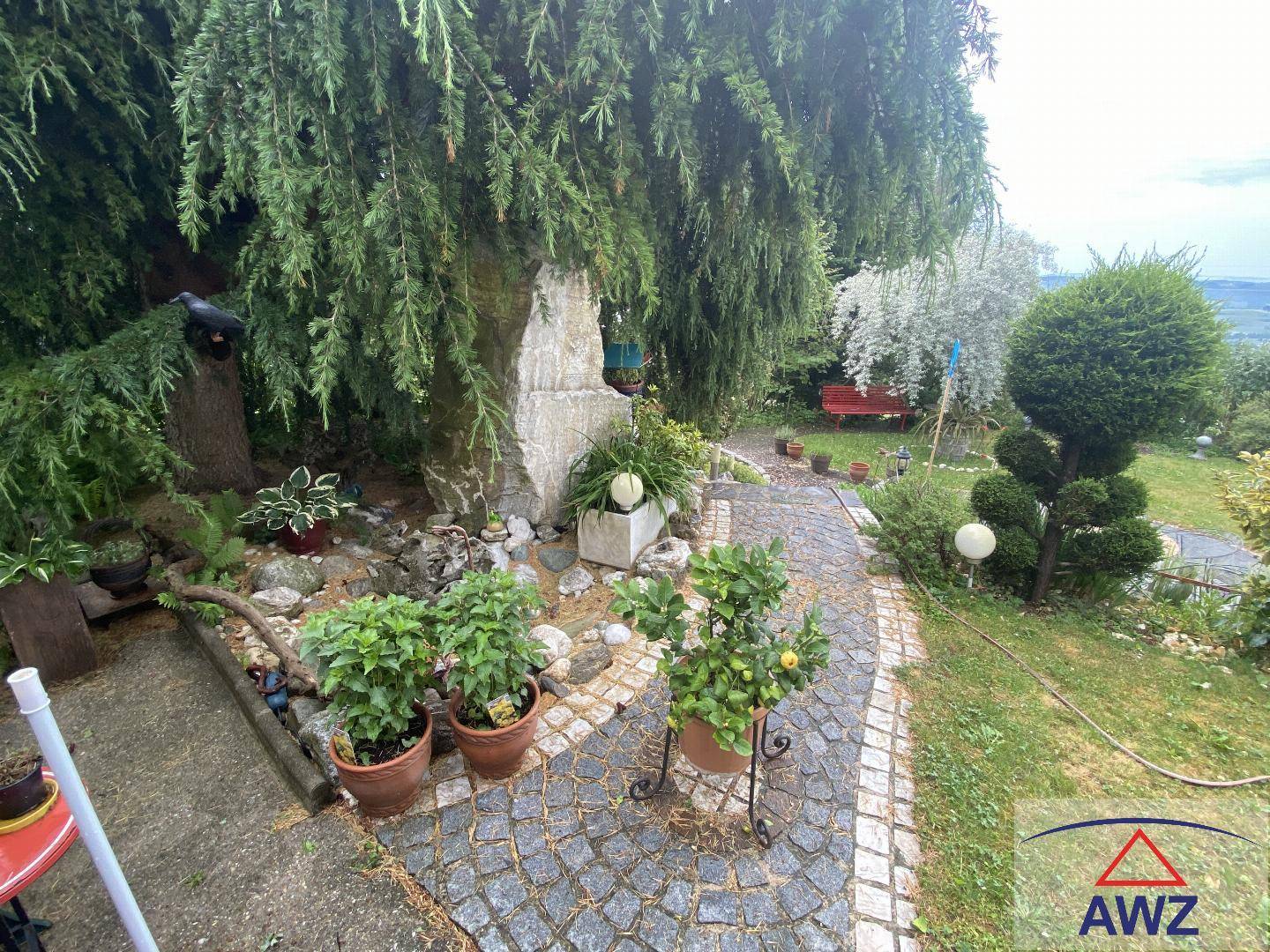 Verwunschener Gartenweg aus Kopfsteinpflaster, umgeben von üppiger Vegetation und Topfpflanzen.