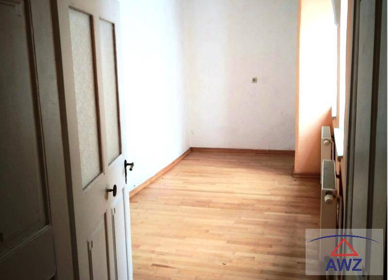 Leeres Zimmer mit hellem Parkettboden, weißen Wänden und Heizkörpern unter dem Fenster.