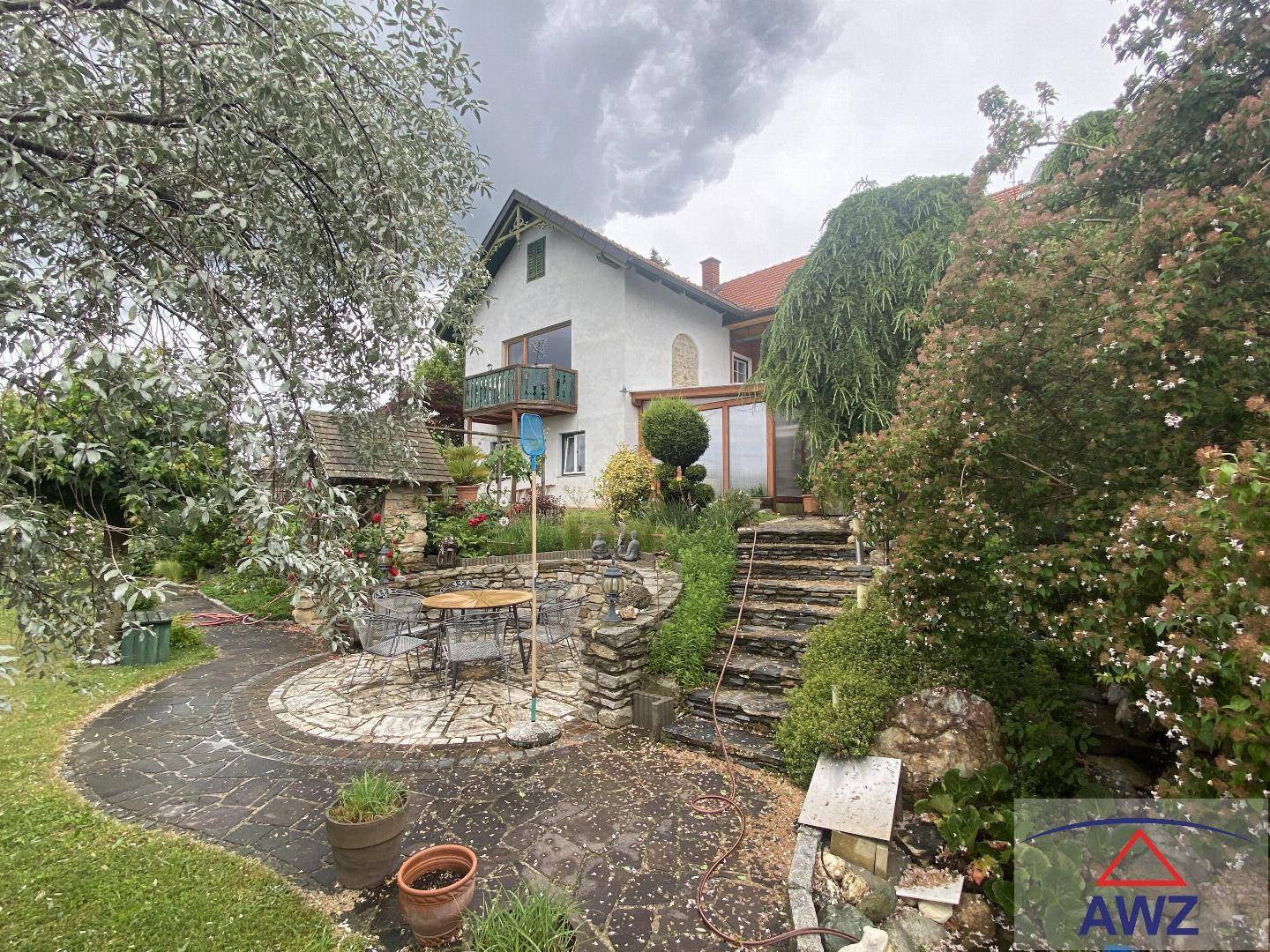 Charmante Terrasse mit Sitzgelegenheiten und Steintreppe, umgeben von einem grünen, bewachsenen Garten.