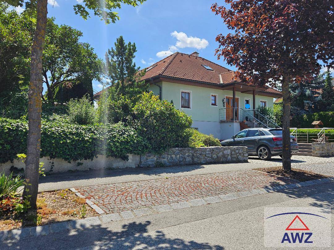Vorderansicht des Hauses von der Straße aus mit gepflastertem Bereich und grüner Hecke.