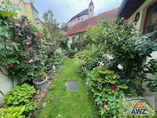 Idyllischer Gartenweg, umgeben von üppigen Pflanzen und Blumen, führt zu einem historischen Gebäude.