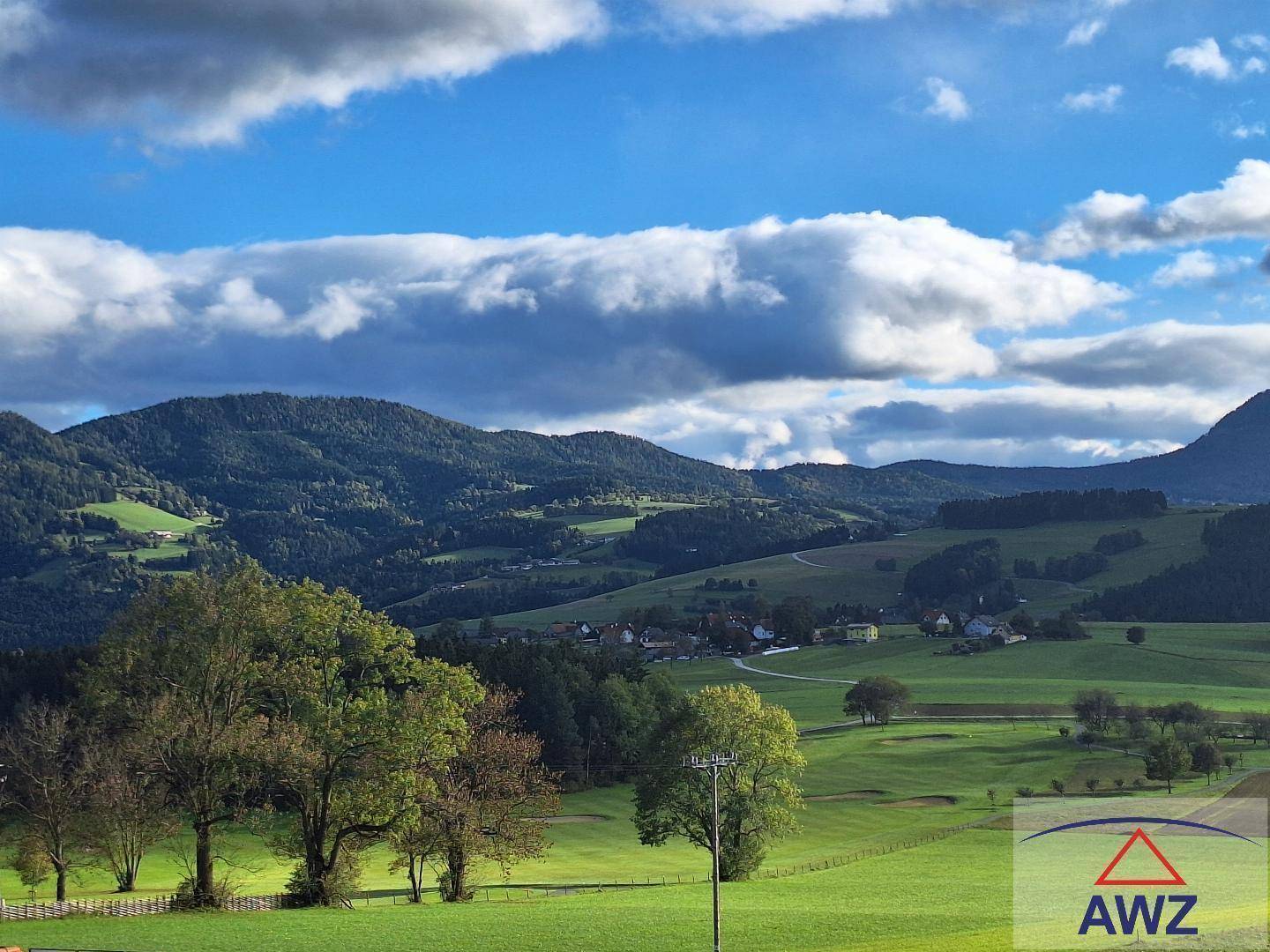 Idyllischer Ausblick auf eine weite grüne Landschaft mit Bergen, Wäldern und einem kleinen Dorf.