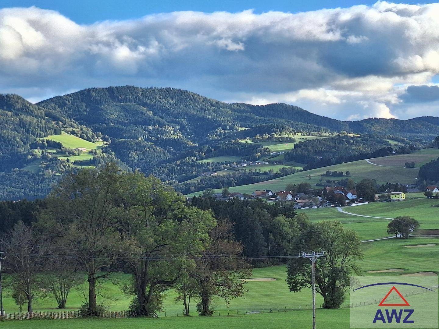 Panoramablick auf eine malerische Berglandschaft mit grünen Hügeln und einem Dorf in der Ferne.