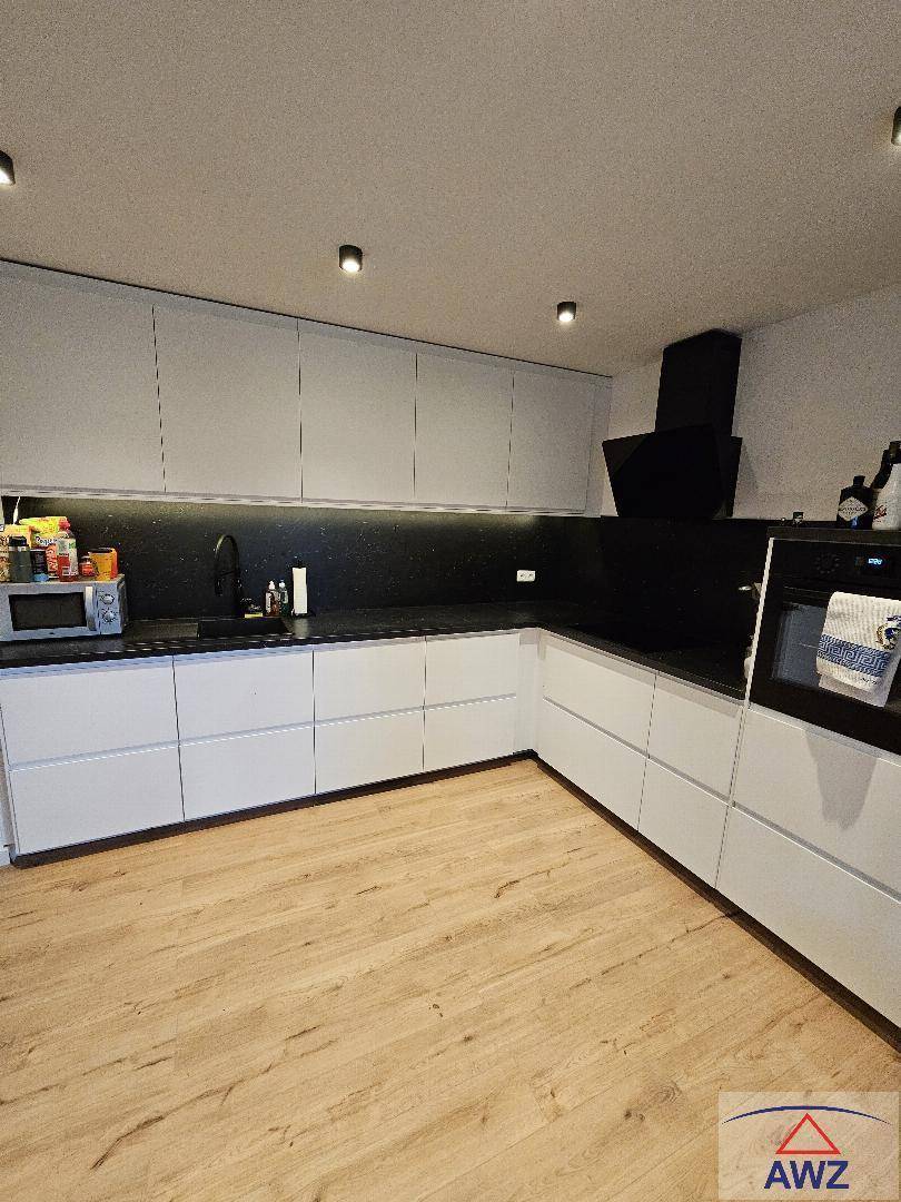 Moderne Küche mit weißen Schränken, schwarzer Arbeitsplatte, integrierten Geräten und Holzboden.