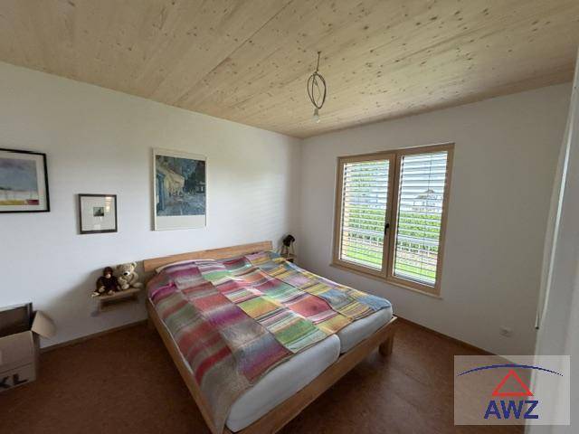 Helles Schlafzimmer mit Holzbett, Holzdecke und Fenster mit Jalousien.