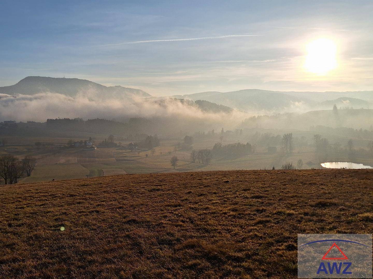 Weitläufige Aussicht auf eine ländliche Gegend mit Nebel, Bergen und einem See bei Sonnenaufgang.