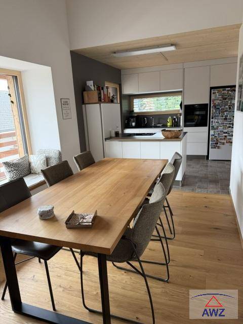 Offener Essbereich mit großem Holztisch und moderner Küche im Hintergrund.