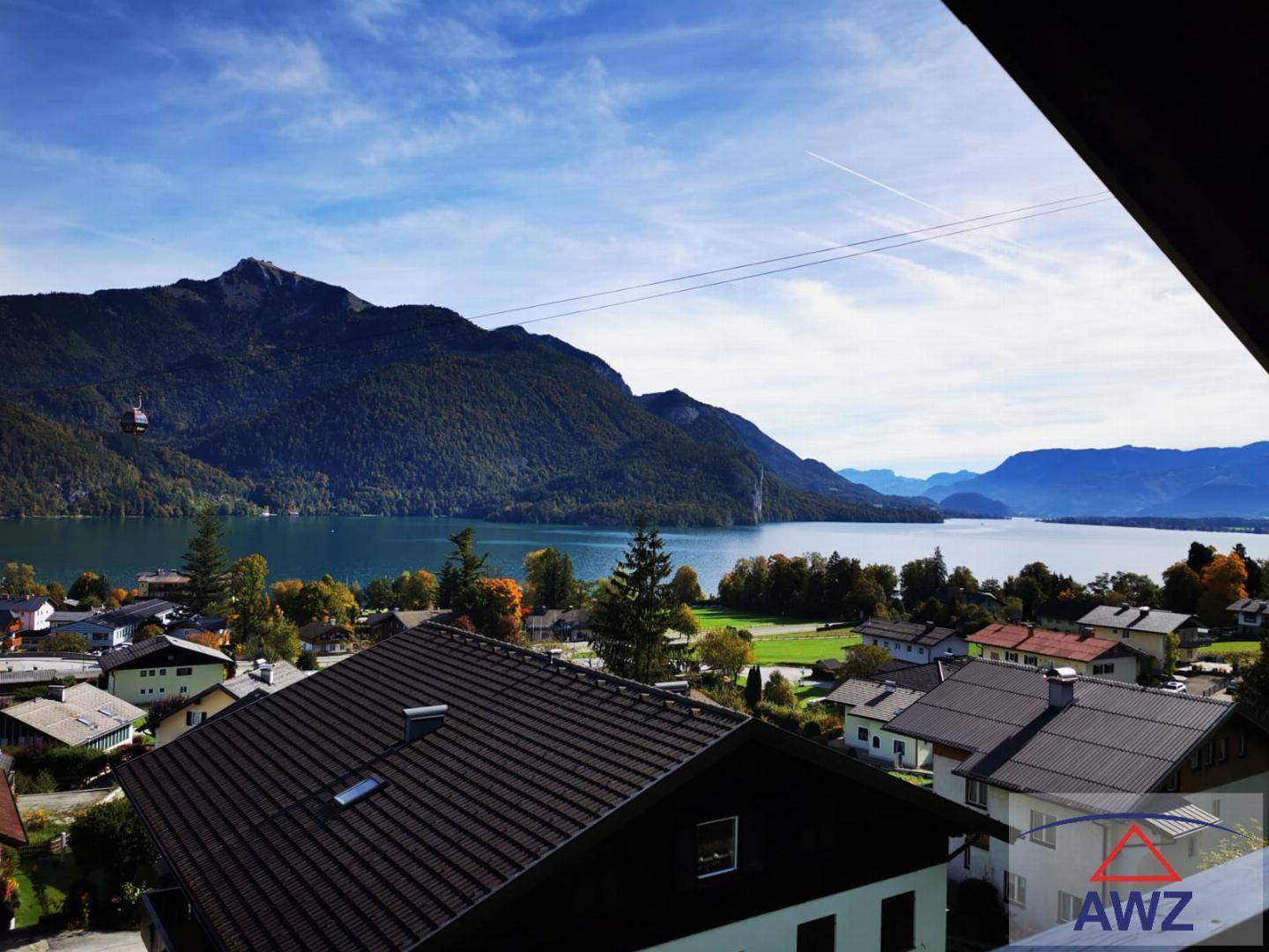 Weitläufiger Blick auf einen idyllischen See, umgeben von bewaldeten Bergen und einer charmanten Ortschaft.