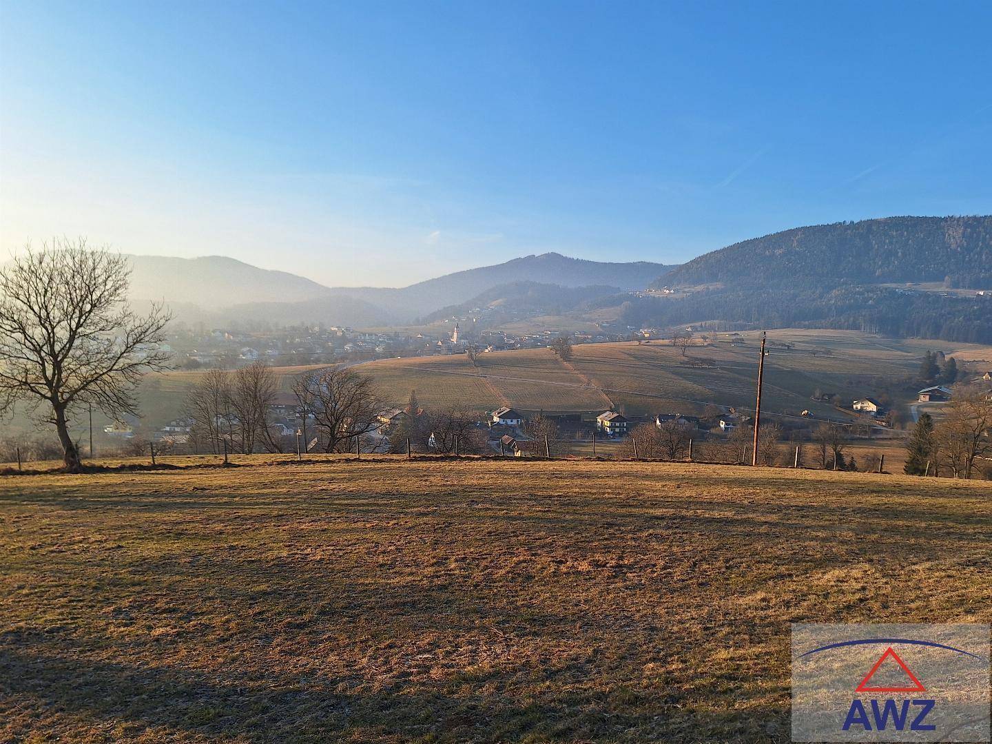 Weitläufiger Blick über eine ländliche Gegend mit einem Dorf und Bergen im Hintergrund.