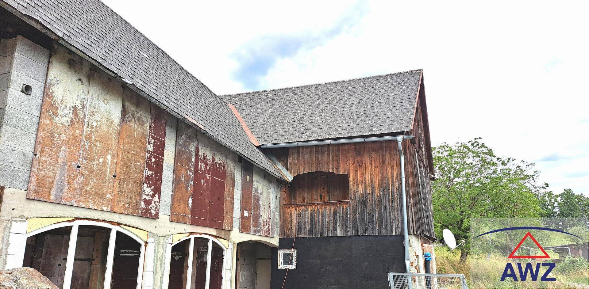 Seite eines alten Gebäudes mit verwitterter Holzfassade und Ziegeldach unter bewölktem Himmel.