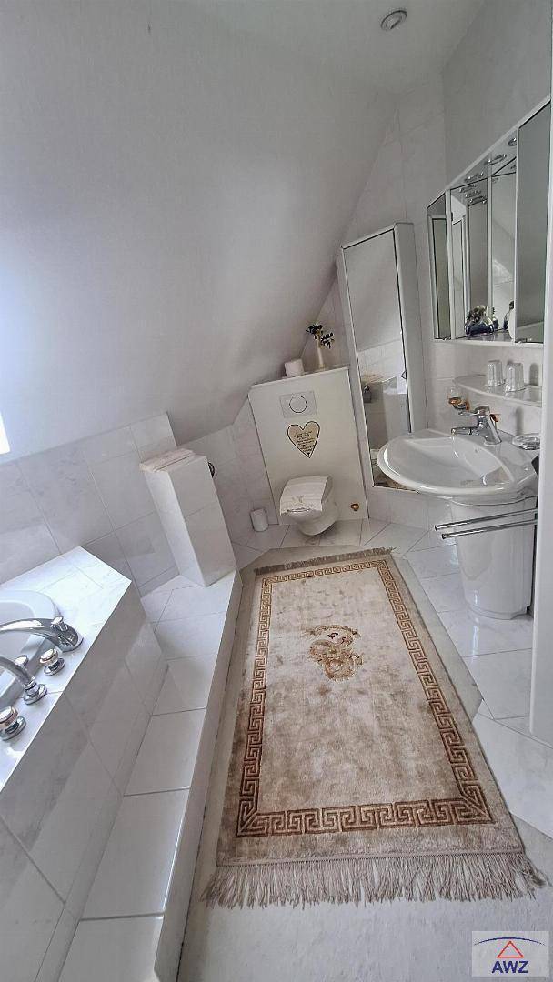Badezimmer mit Waschbecken, Toilette, Spiegelschrank und Badewanne unter einer Dachschräge.