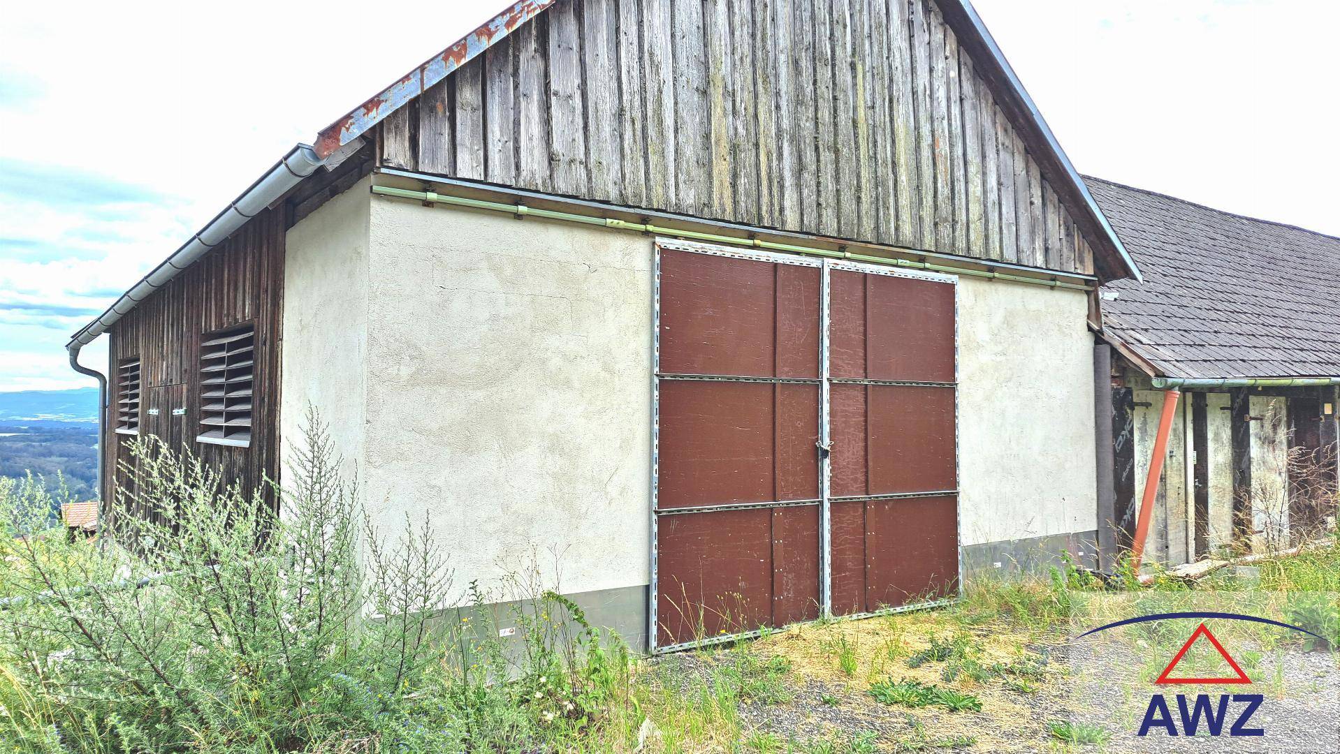 Altes Nebengebäude mit Holzwänden und großen braunen Türen in ländlicher Umgebung, rustikaler Charme.