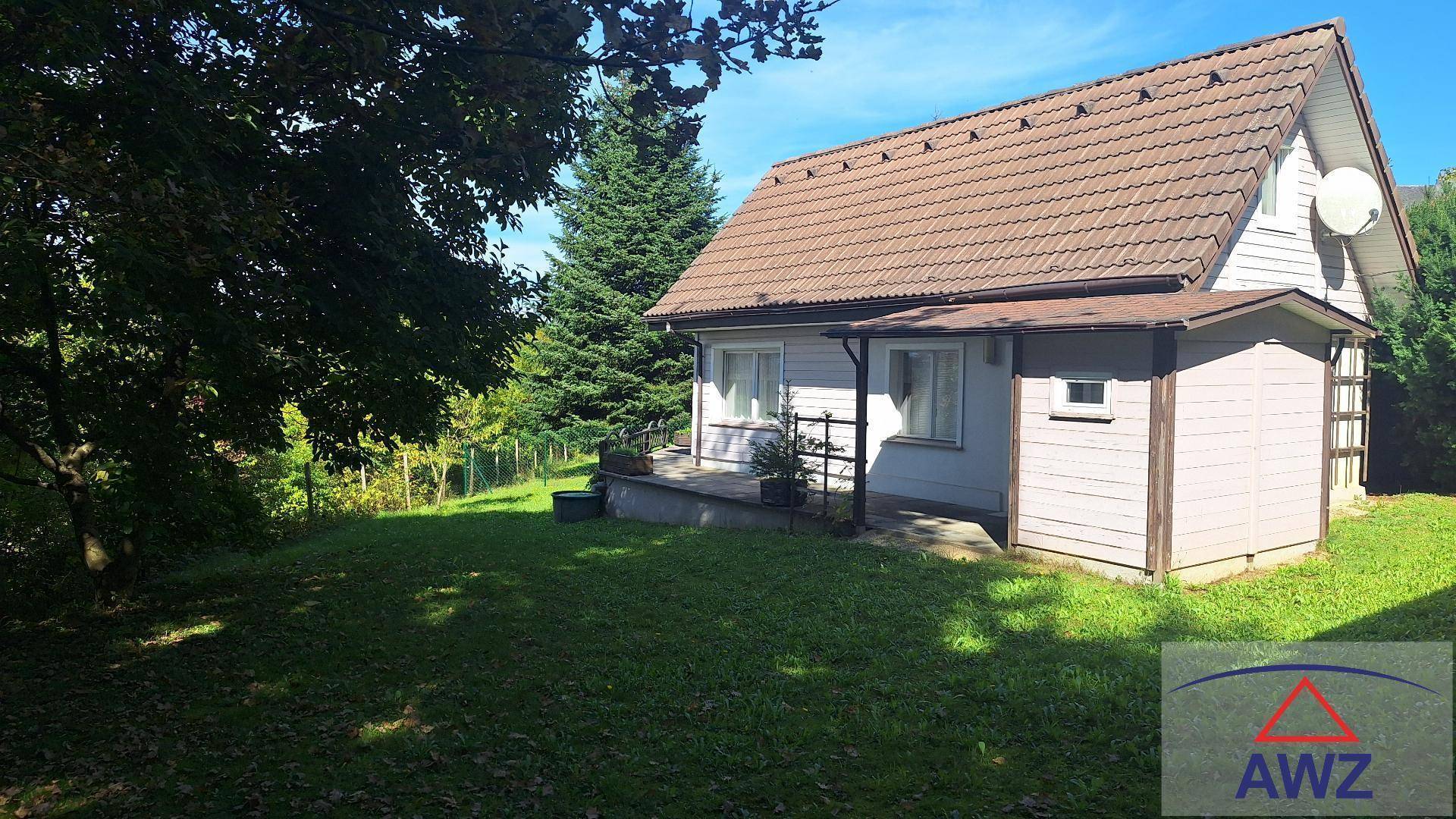 Kleines Haus mit Satteldach und umliegendem Garten, eingebettet in eine grüne Landschaft.