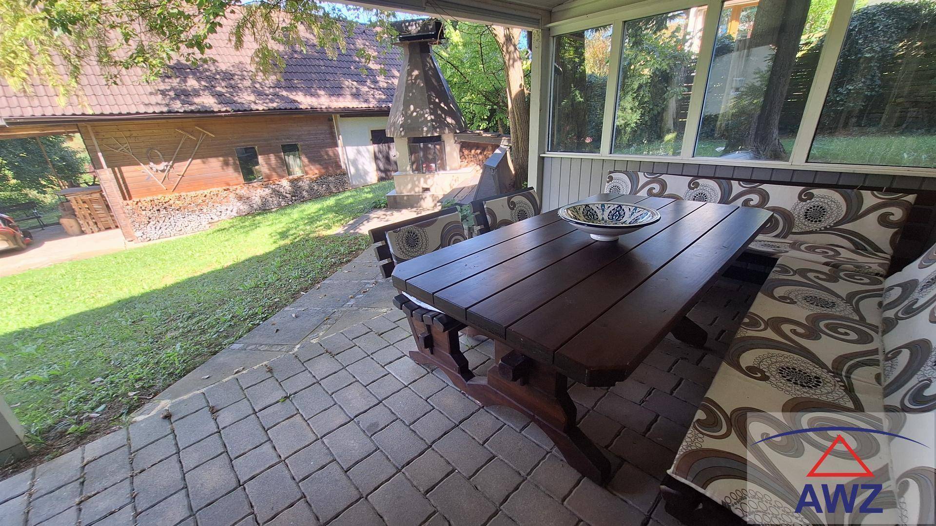 Überdachte Terrasse mit rustikalen Holzmöbeln und Blick auf den Garten mit Grillplatz.