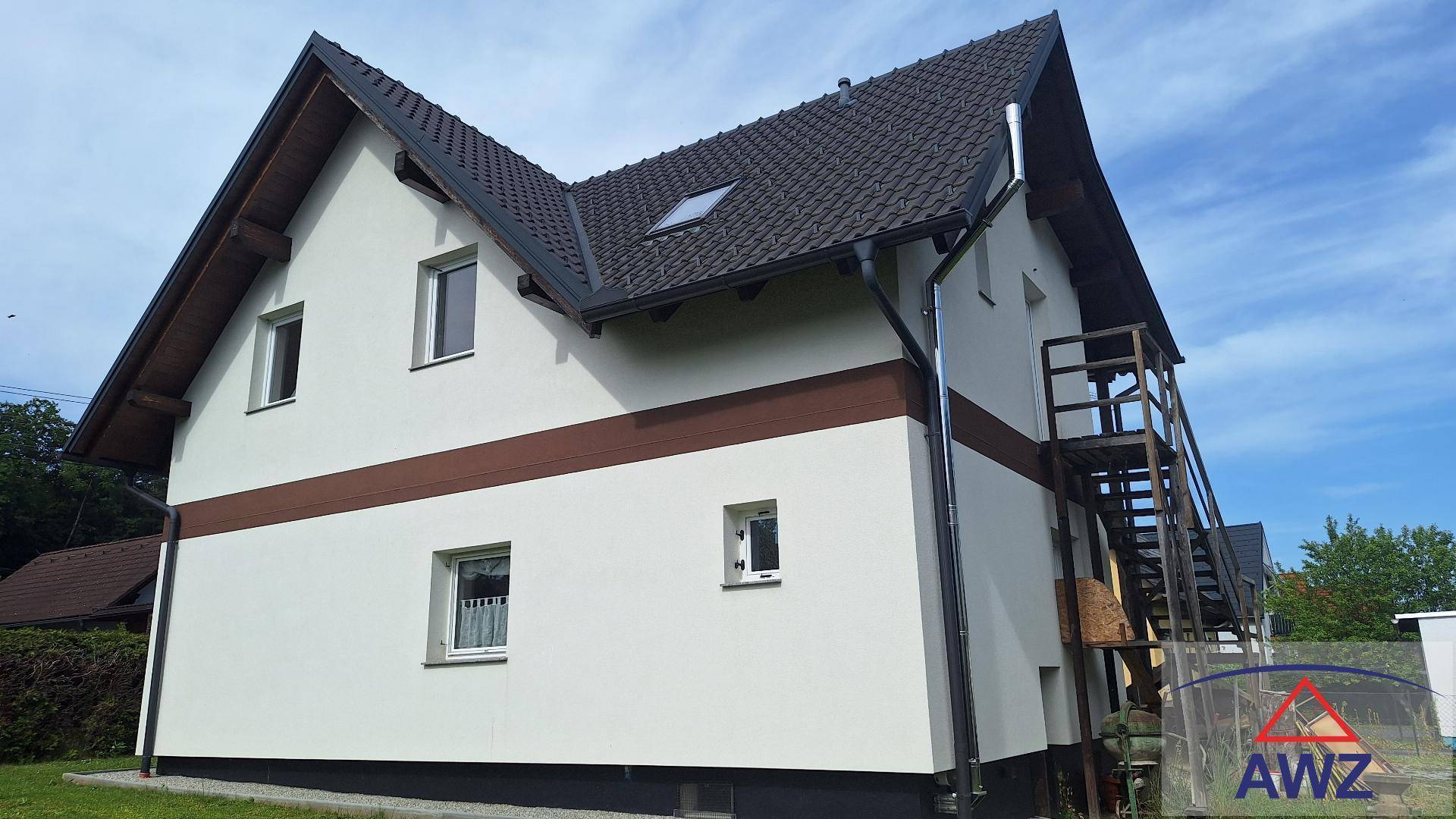 Ansicht der Hausfassade mit weißem Putz, braunem Band und dunklem Satteldach sowie einer Außentreppe.