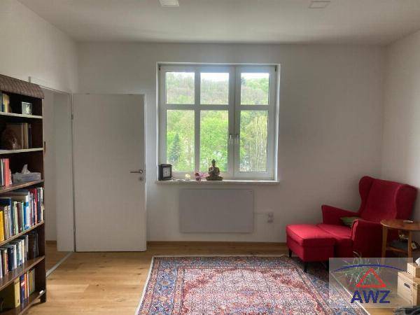 Helles Wohnzimmer mit Holzboden, rotem Sessel und einem großen Fenster mit Blick ins Grüne.