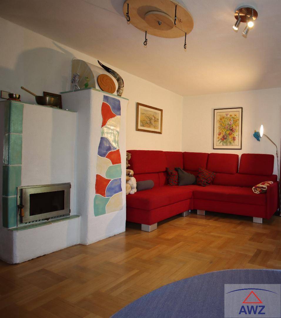 Helles Wohnzimmer mit rotem Ecksofa und einem dekorativen Kachelofen.