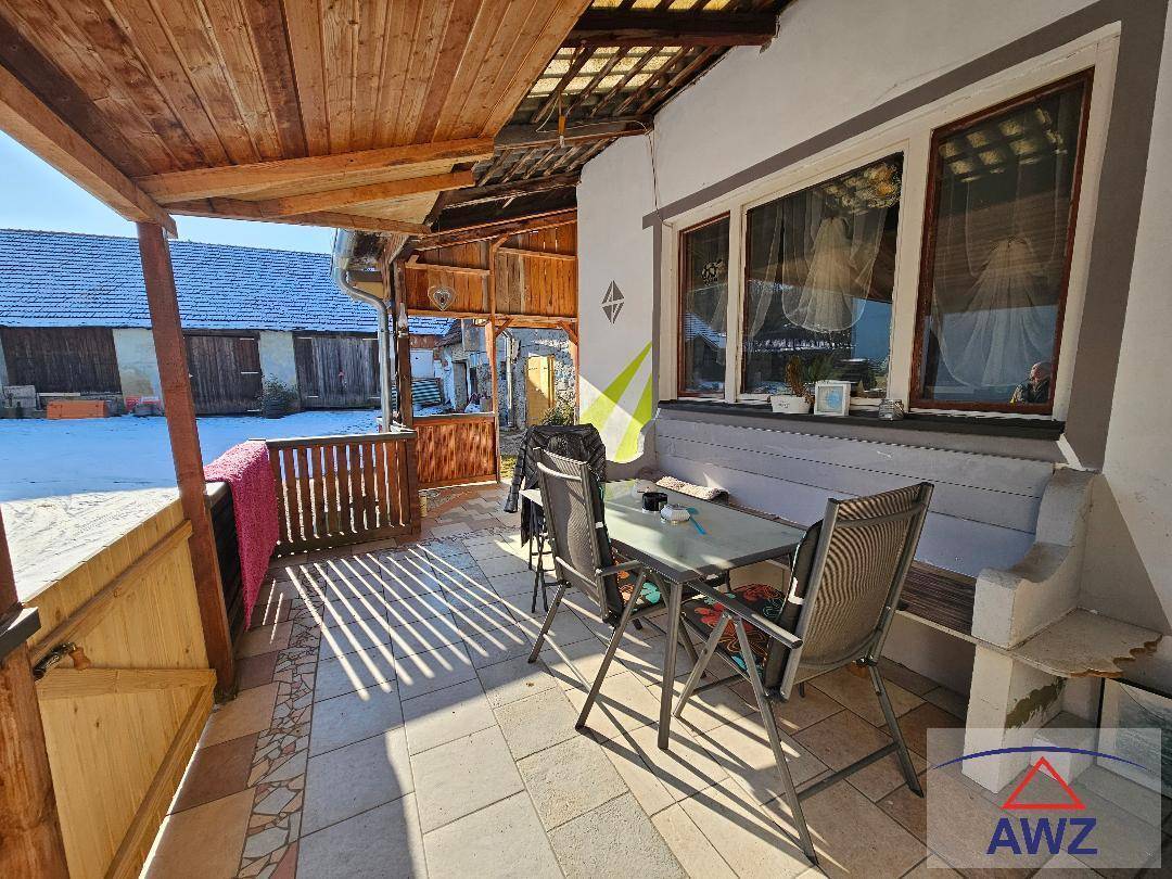 Überdachte Terrasse mit Holzbalken, Fliesenboden und Sitzgelegenheiten, Blick auf verschneite Umgebung.