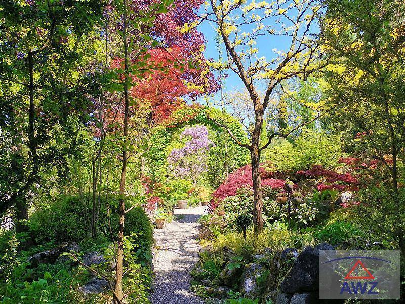 Wunderschöner, üppiger Garten mit Kiesweg, farbenfrohen Bäumen und blühenden Pflanzen.