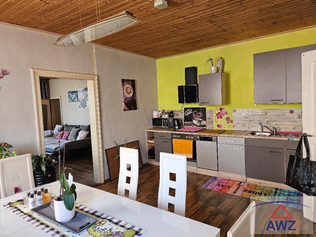 Offene Küche mit grauen Schränken und einer hellgrünen Wand, kombiniert mit einem Essbereich.