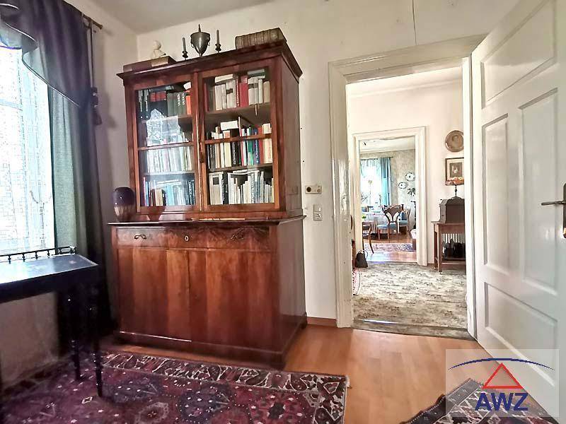 Gemütliches Wohnzimmer mit großem Holzregal, dunklem Teppich und Blick in einen weiteren Raum.