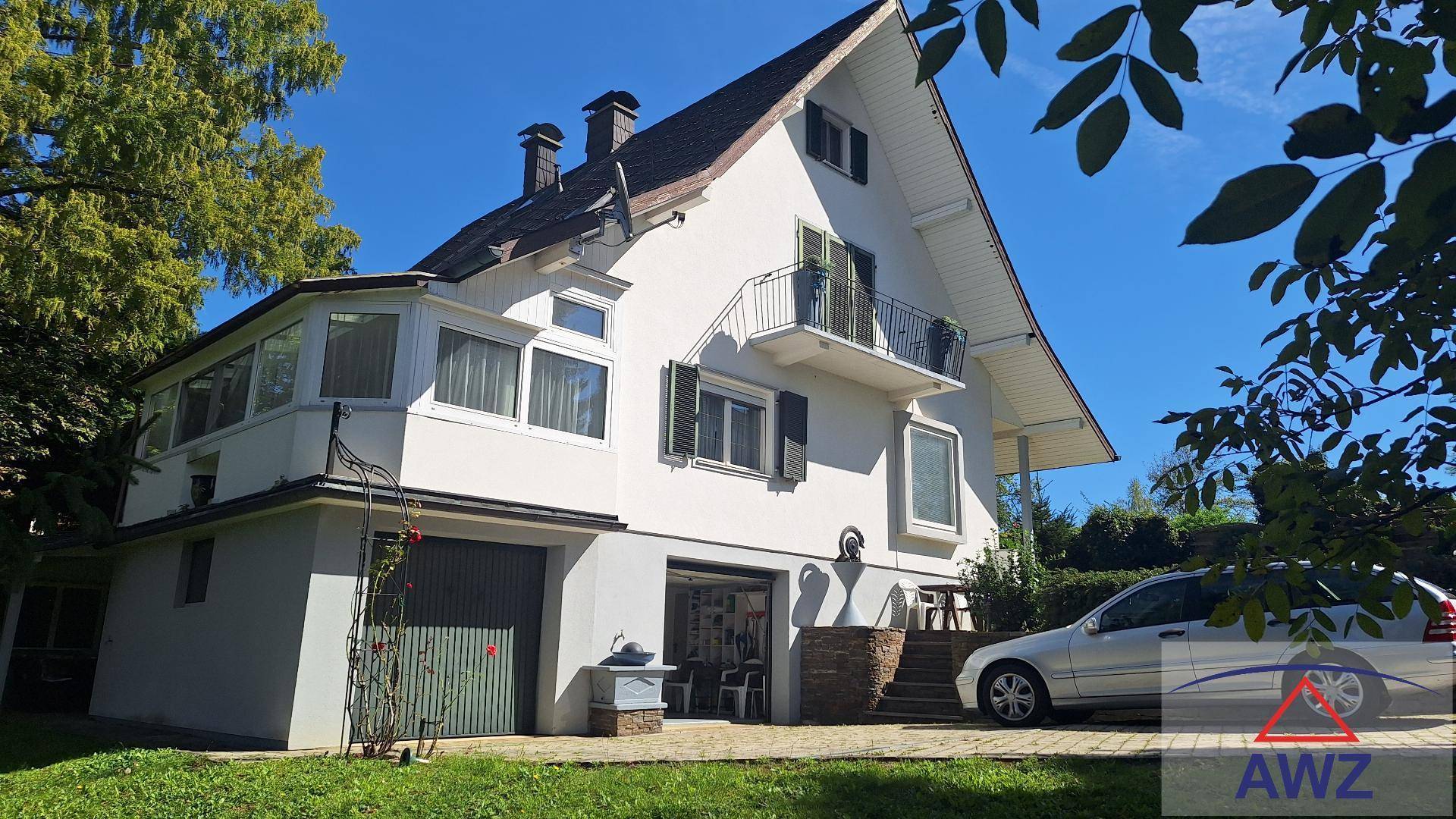 Freistehendes Haus mit Garage, Balkonen und gepflegtem Garten unter blauem Himmel.