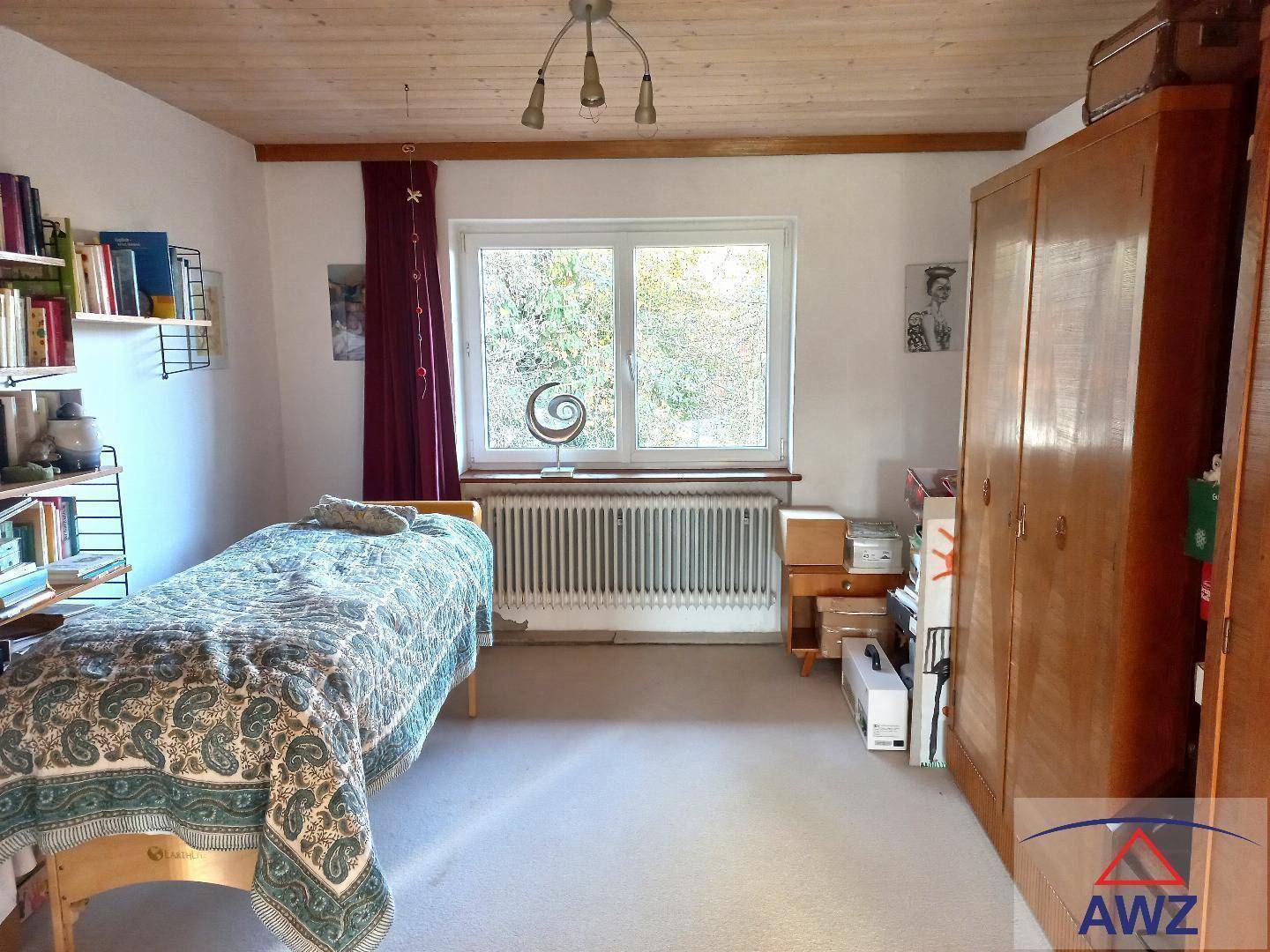 Schlichtes Schlafzimmer mit Einzelbett, Holzschrank und Blick ins Grüne.