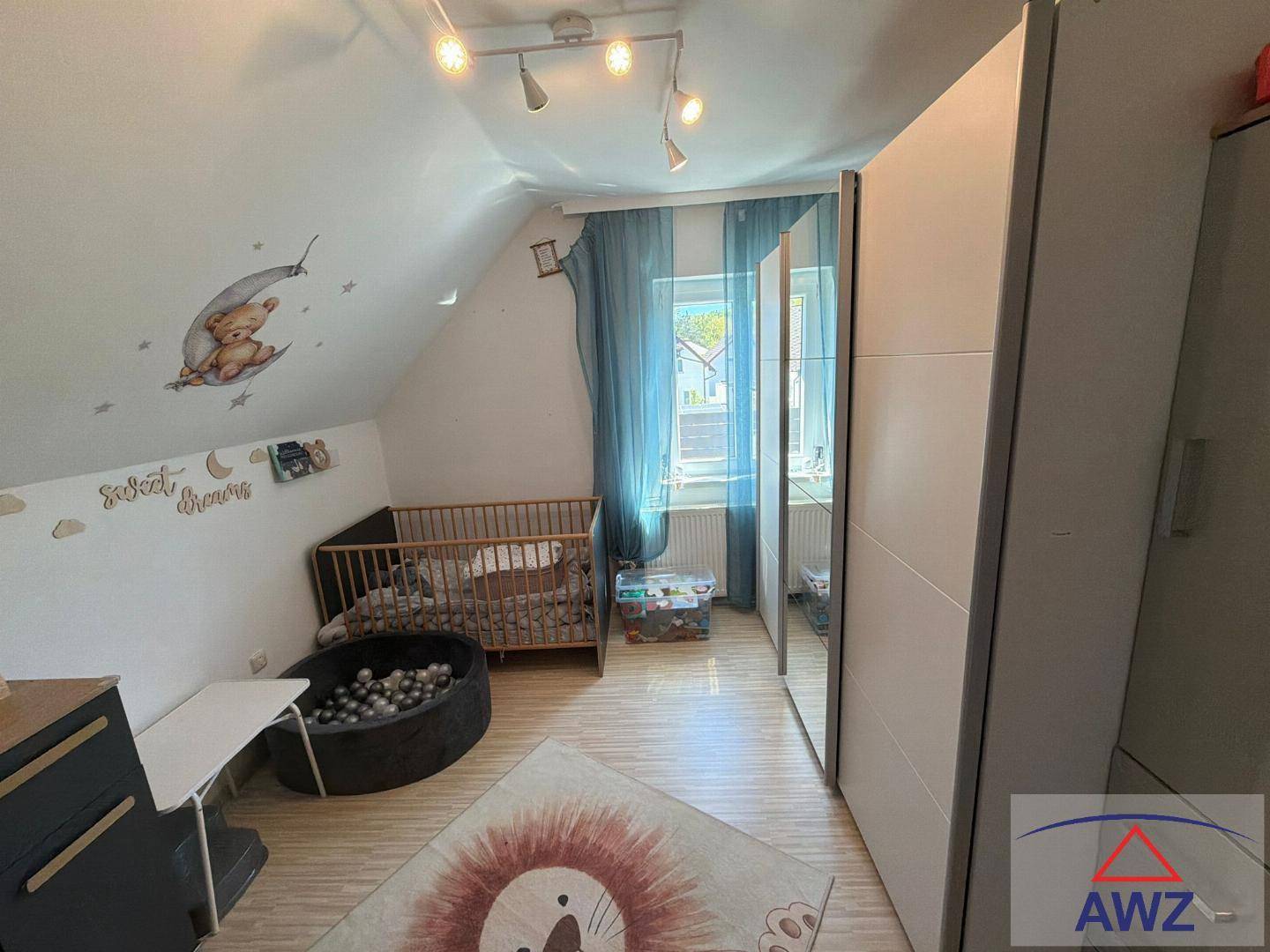 Helles Kinderzimmer mit Babybett, Spielbereich und Schrank unter einer Dachschräge.