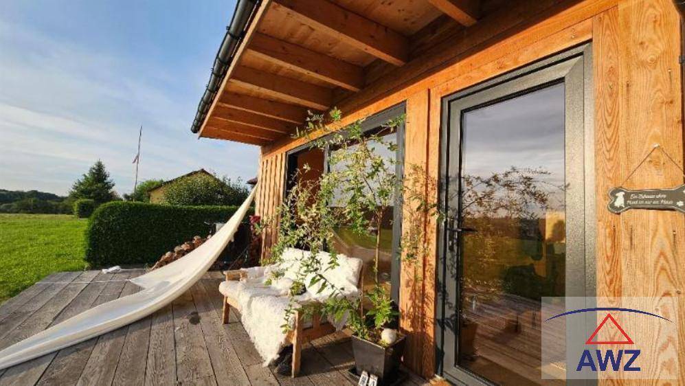 Gemütliche Holzterrasse mit Sitzgelegenheiten und Hängematte vor einer Holzhütte mit weitem Blick ins Grüne.