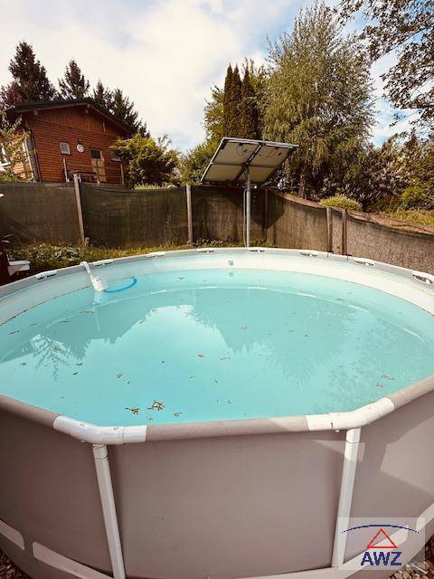 Runder Aufstellpool im Garten mit Solarmodulen und einem kleinen Holzhaus im Hintergrund.