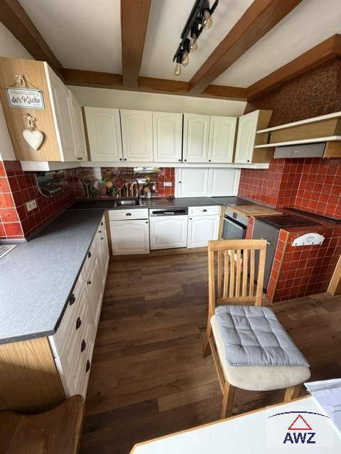 Gemütliche Küche mit weißen Schränken, roten Fliesen und sichtbaren Holzdeckenbalken.