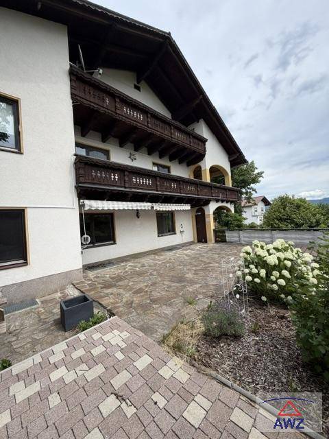 Traditionelles Haus mit mehreren Holzbalkonen und einer gepflasterten Terrasse im Außenbereich.