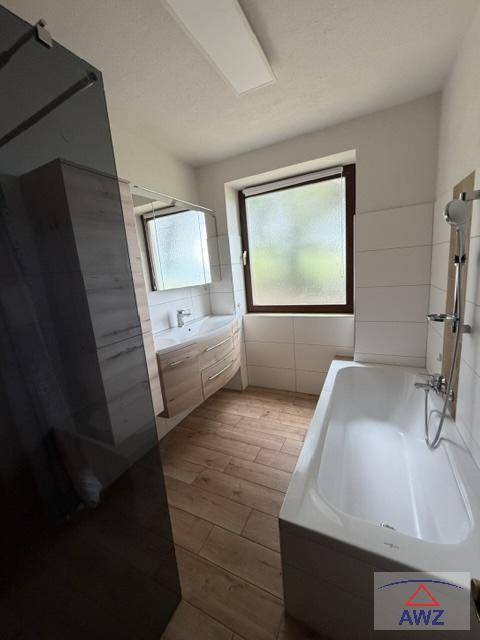 Helles Badezimmer mit Badewanne, modernem Waschtisch und Fenster für Tageslicht.