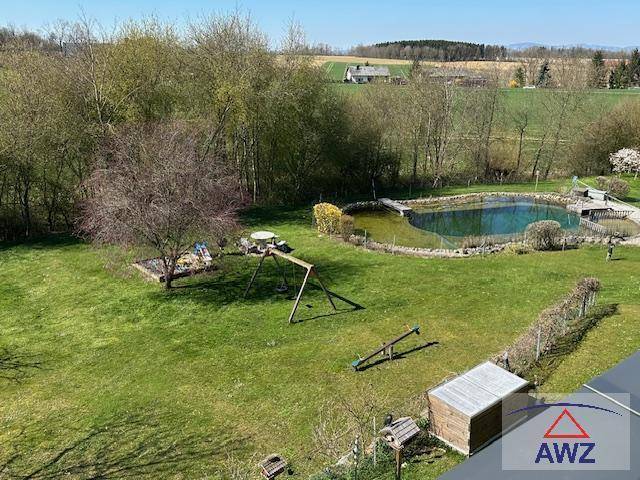 Großer Gartenbereich mit natürlichem Teich, Spielplatz und weitem Blick auf die umliegende Landschaft.