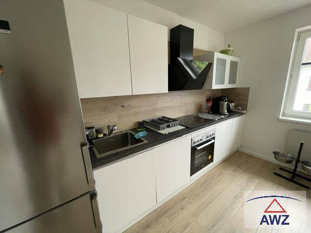 Moderne Küche mit weißen Schränken, integriertem Backofen und Edelstahlkühlschrank.