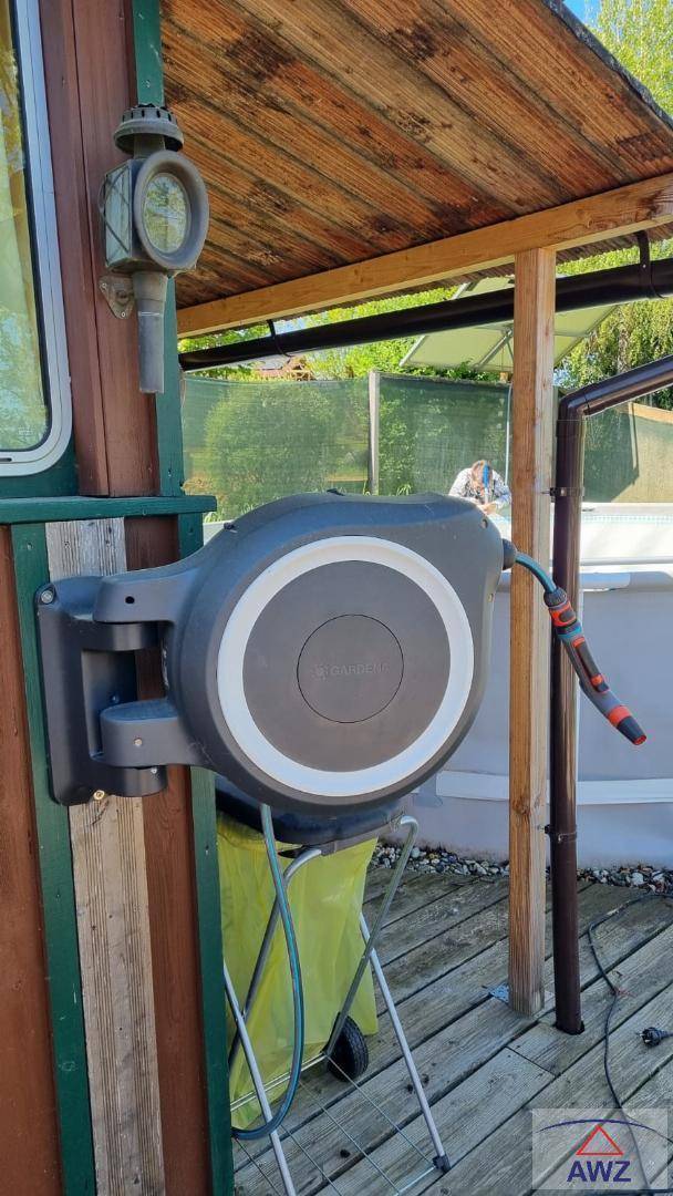 Wandmontierte Gartenschlauchrolle an einem Holzhaus unter einem kleinen Vordach, praktisch für den Garten.