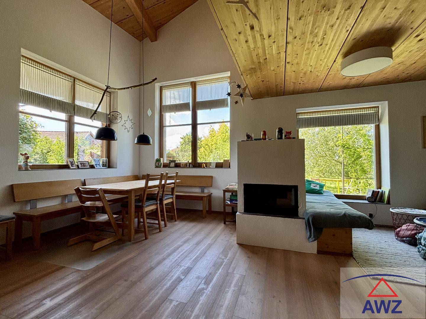 Heller Wohn-Essbereich mit Kamin, Holzboden und großen Fenstern mit Blick ins Grüne.