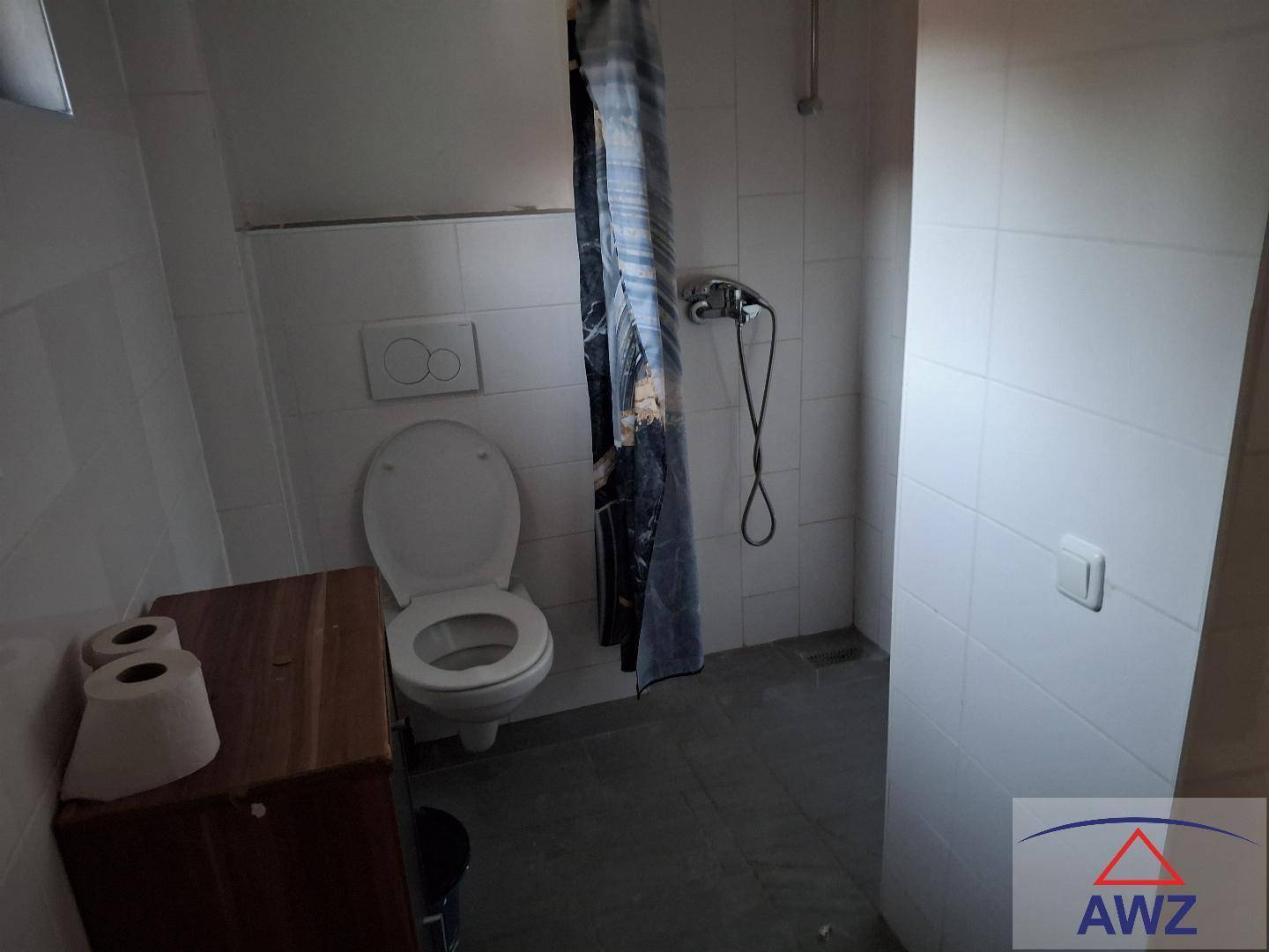 Ein einfaches Badezimmer mit weiß gefliesten Wänden, einer Toilette und einem Duschbereich mit Vorhang.