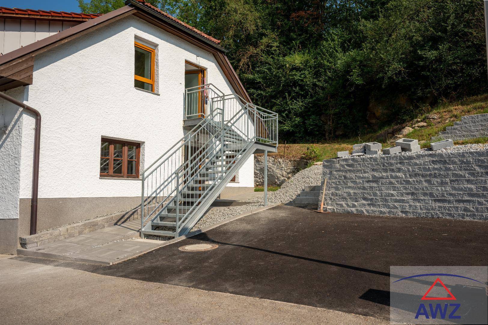 Außenansicht eines Hauses mit weißer Fassade, Außentreppe und Hanglage.