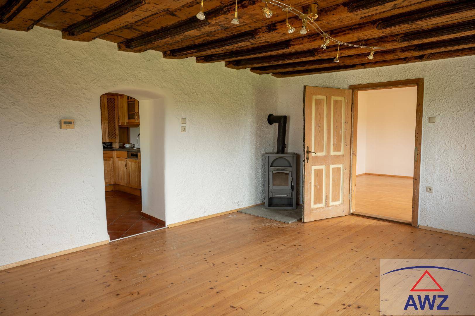 Rustikales Wohnzimmer mit Holzbalkendecke, Dielenboden und gemütlichem Holzofen.