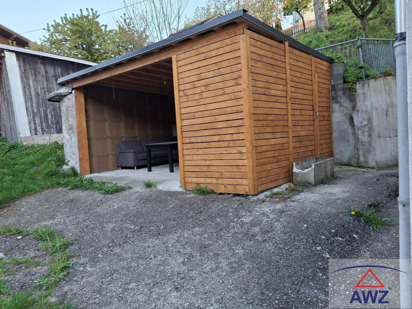 Ein offener Holzunterstand, der als Carport oder Gartenhaus mit Sitzgelegenheiten genutzt werden kann.