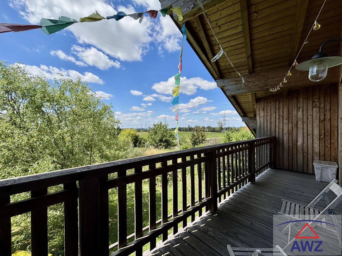 Holzbalkon mit weitem Blick auf die grüne Landschaft unter einem strahlend blauen Himmel.